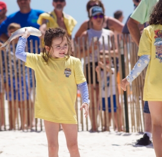 Young girl throwing a fish at Flora-Bama's Annual Mullet Toss in Orange Beach