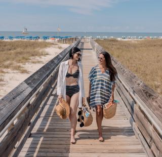 Two girlfriend's enjoying a trip together while walking on a boardwalk with scenic views on Alabama's Beaches
