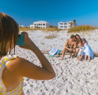 Young girl taking a photo of her family with a blue camera on the beach